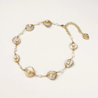 Gold-plated necklace with wire-wrapped shell pieces and freshwater pearls on neutral background, adjustable chain visible.