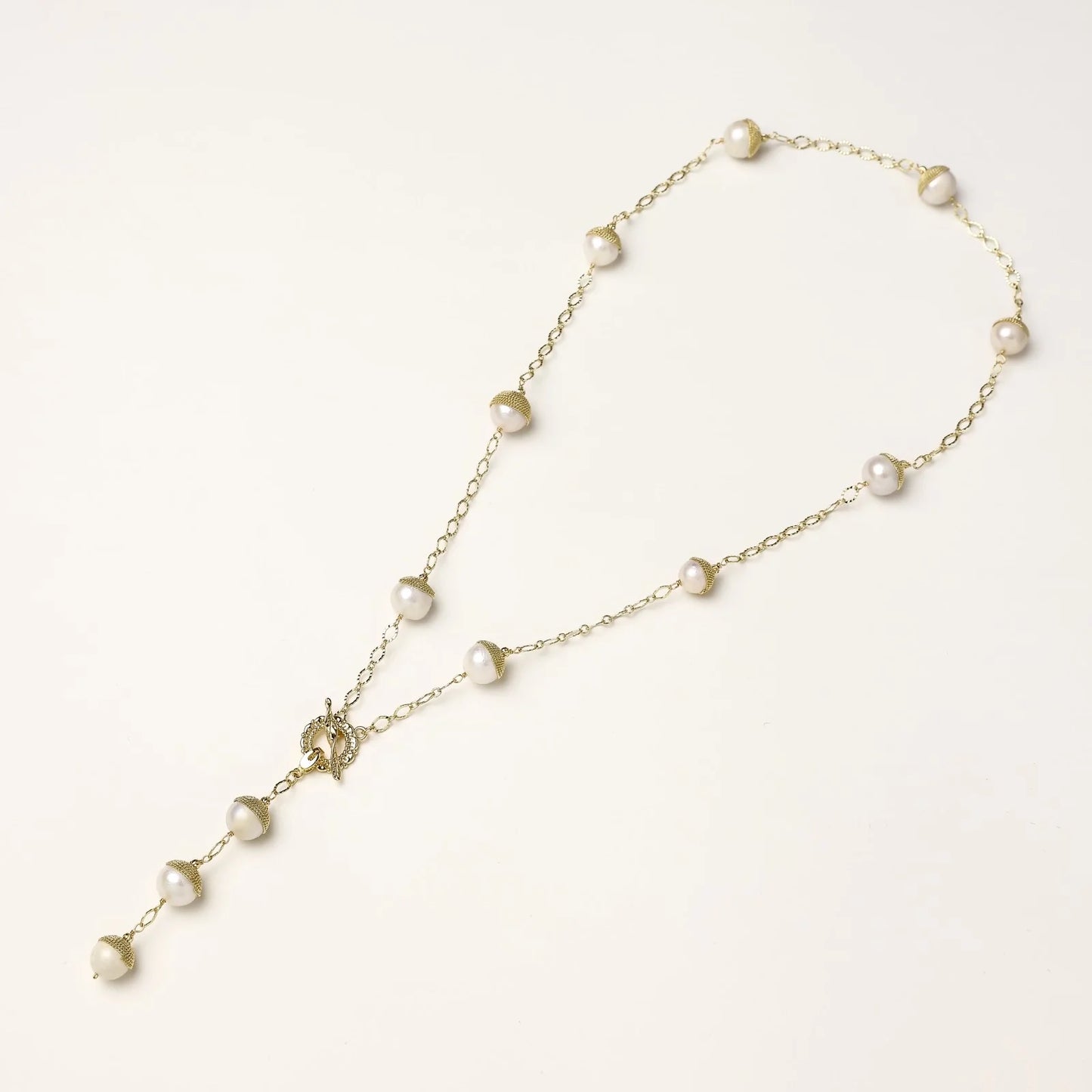 Gold-plated lariat necklace with baroque pearls and textured caps on cream background, showing adjustable Y-shaped design.