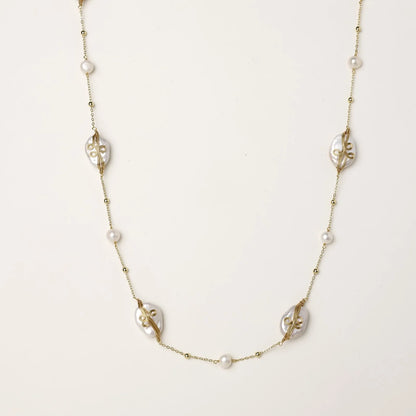 Long gold chain necklace with baroque pearls wrapped in leaf designs and small freshwater pearls spaced along the strand