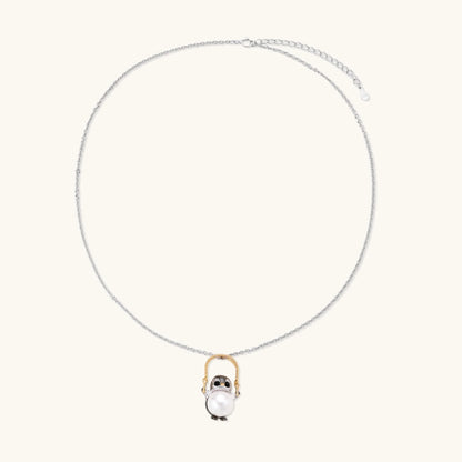 Whimsical owl pendant holding a white pearl on a gold swing, rhodium-plated silver chain on cream background.