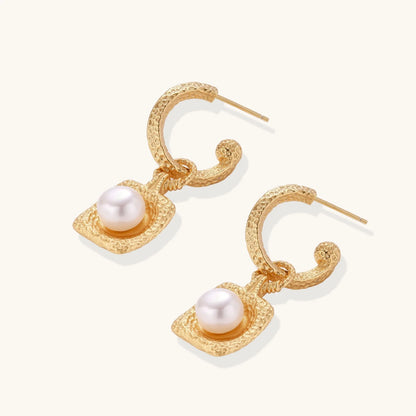 Pair of gold vermeil hoop earrings with textured square frames holding freshwater pearls on cream background