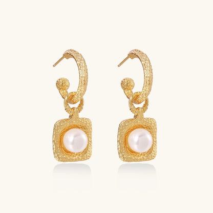 Pair of gold vermeil hoop earrings with textured square frames holding freshwater pearls on cream background