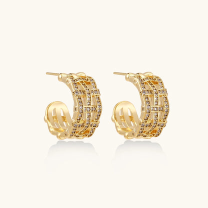 Gold-plated geometric hoop earrings with basket-weave lattice design and pavé crystal accents on cream background
