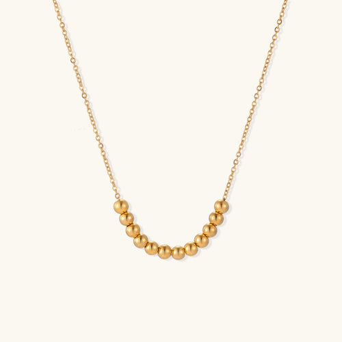 Delicate gold-plated necklace with graduated spherical beads forming gentle smile curve on beige background
