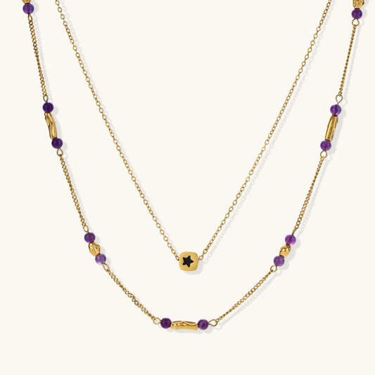 Two layered gold-tone necklaces with purple stone beads and star pendant against cream background.