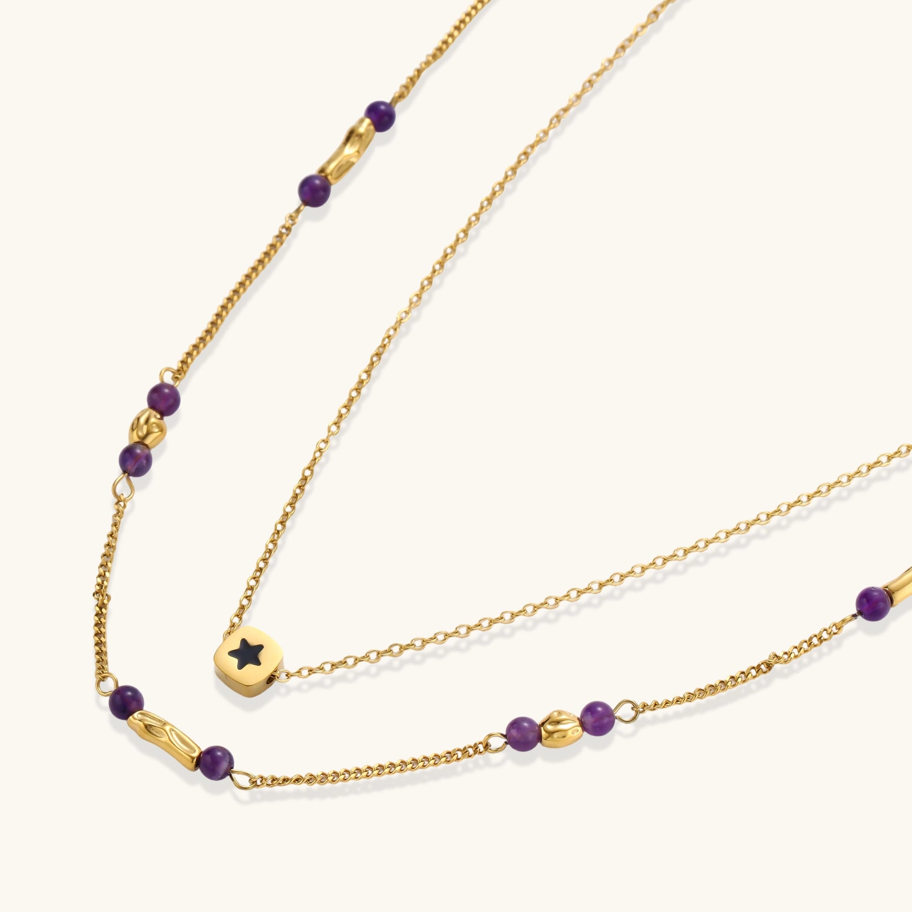 Two layered gold-tone necklaces with purple stone beads and star pendant against cream background.